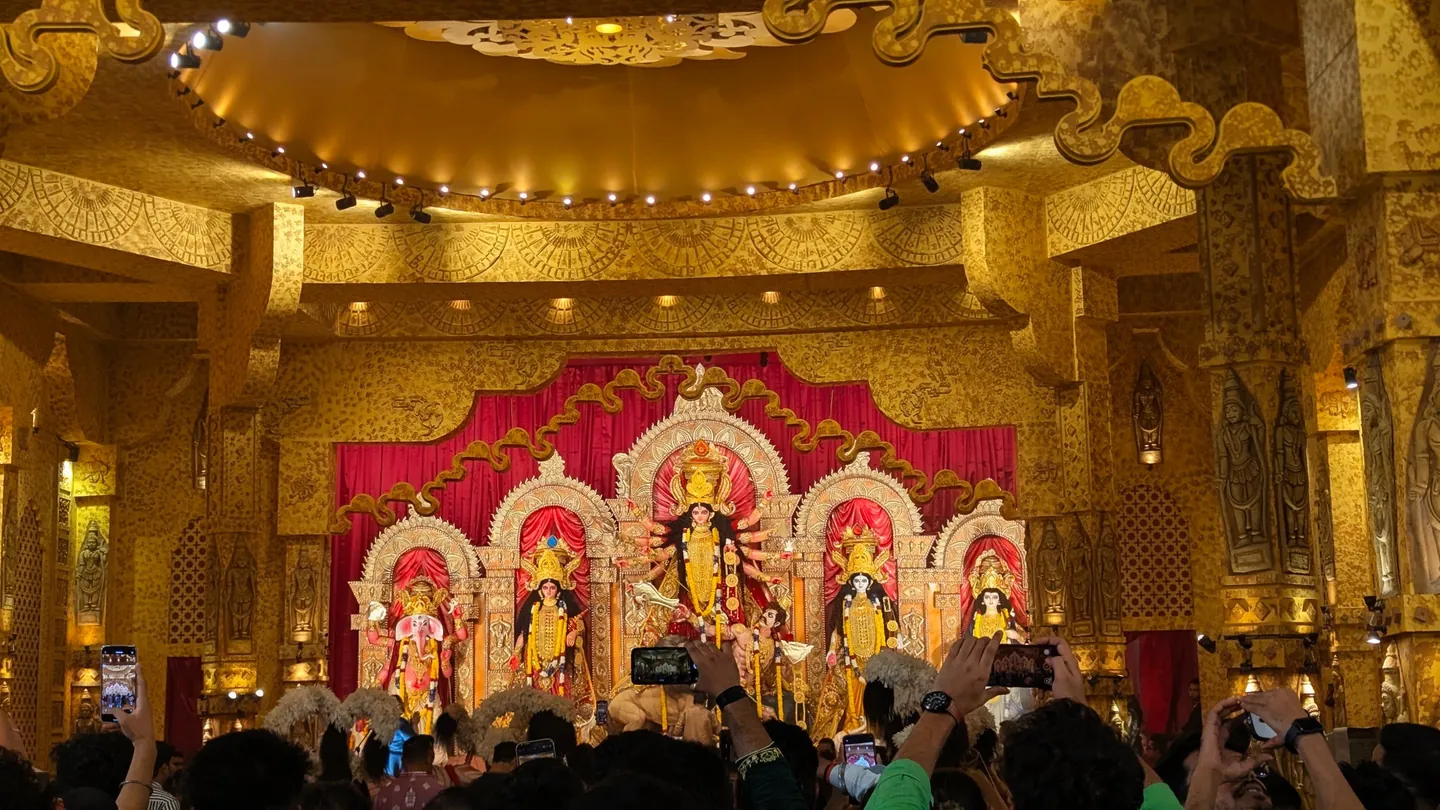 Durga and accompanying figures in an ornate gold pandal, with visitors in the foreground