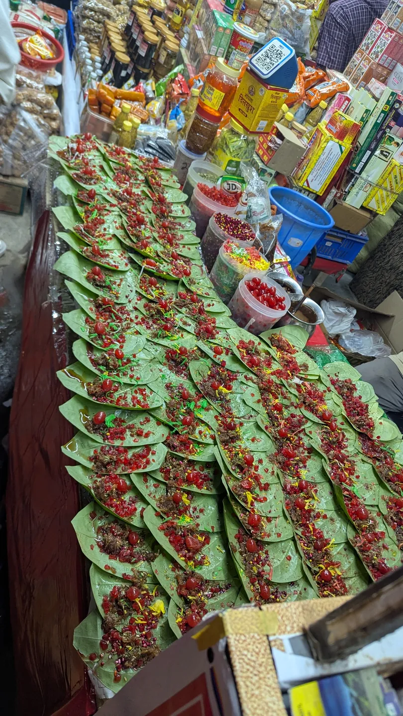 Rows of green paan leaves topped with colourful ingredients at a market stall