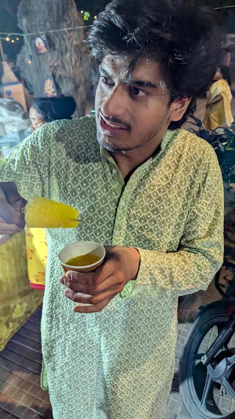 A guest in a green kurta holding a cup at a busy street-food stall